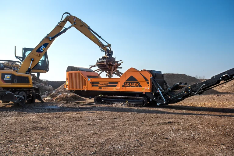 An orange Doppstant AK 640 grinder is loaded with waste wood to be ground into wood chips.