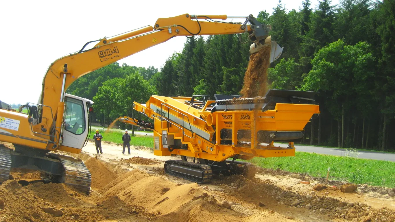 A yellow environmental processing machine separates material into different sized piles.