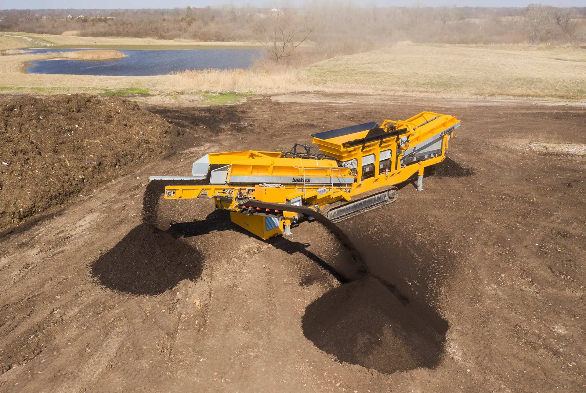 A yellow Backers star screen machine with conveyors extended separates material into two piles.