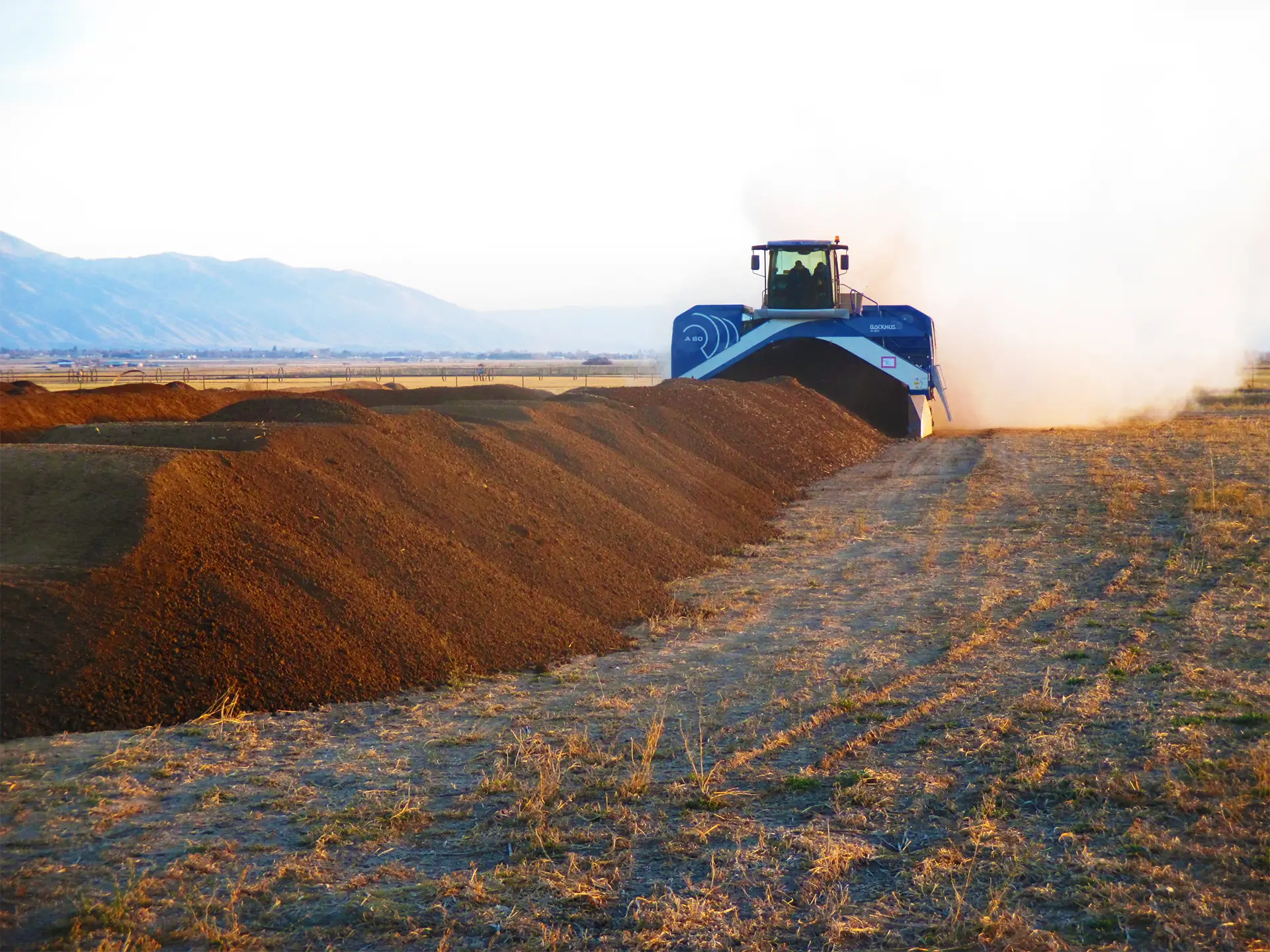 A BACKHUS compost turner makes its way down a long compost windrow, turning it as it moves.