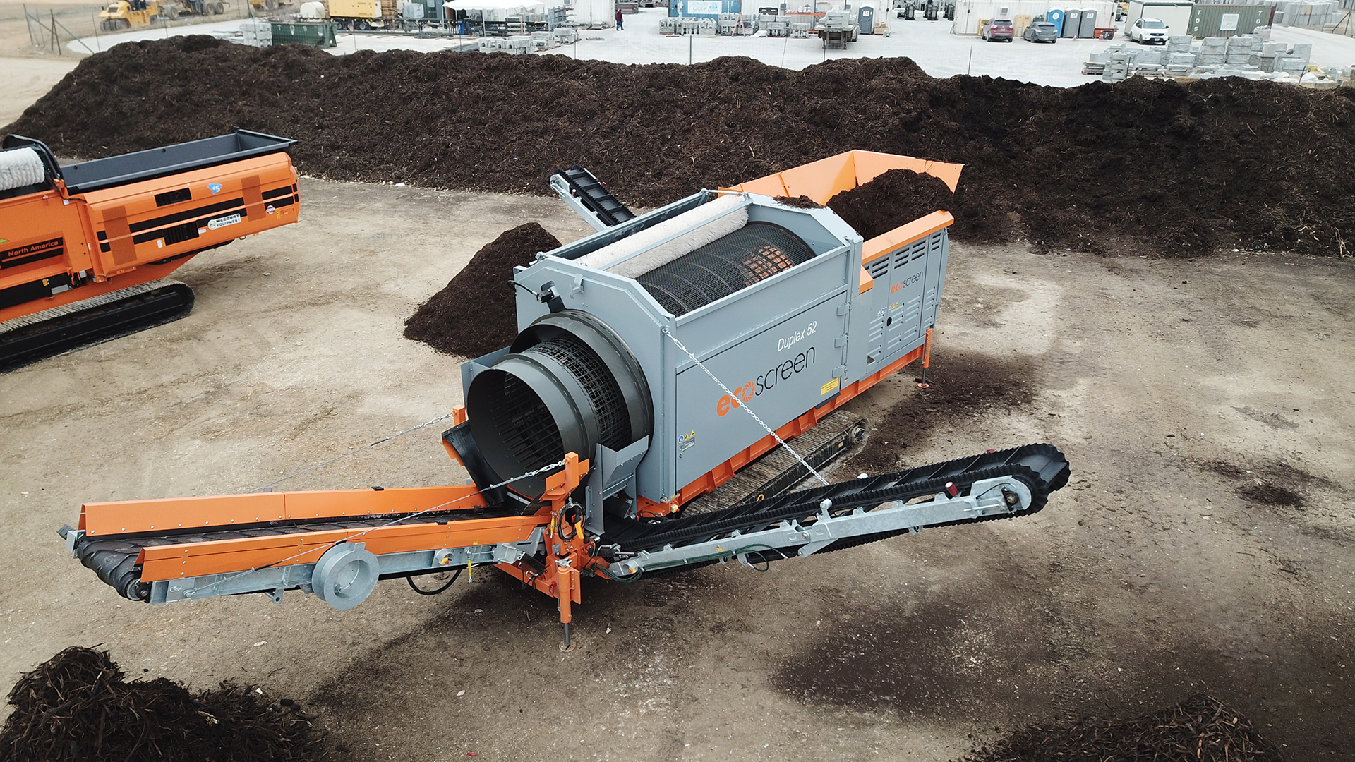 The gray and orange EcoScreen Duplex 52 trommel screen is separating mulch into different sized piles.