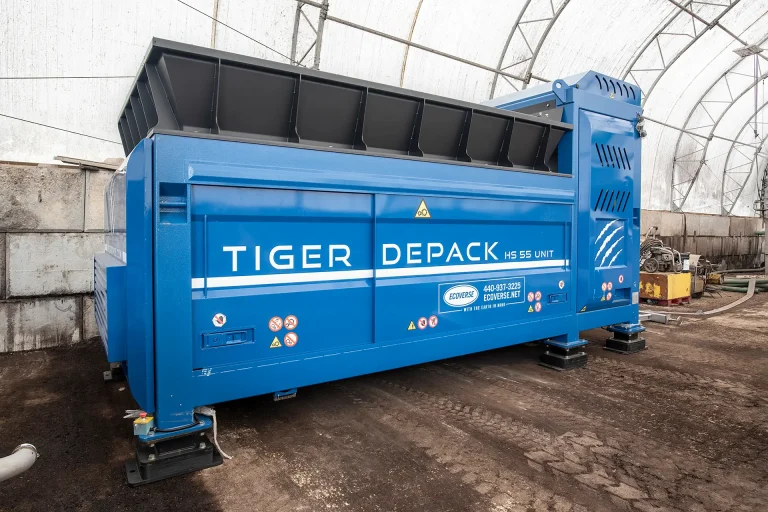 A blue Tiger Depack HS-55 waste food processing machine sits in a covered facility with a dirt floor.