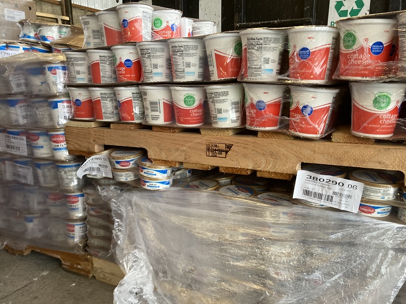 Large containers of expired food products are wrapped in clear plastic and sitting on pallets.