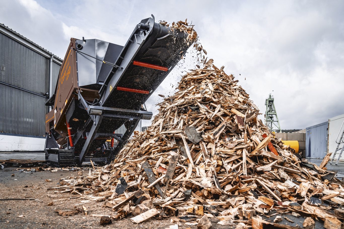 A CoreShred 250 shredder is seen from ground level as shredded wood is discharged from its main conveyor.