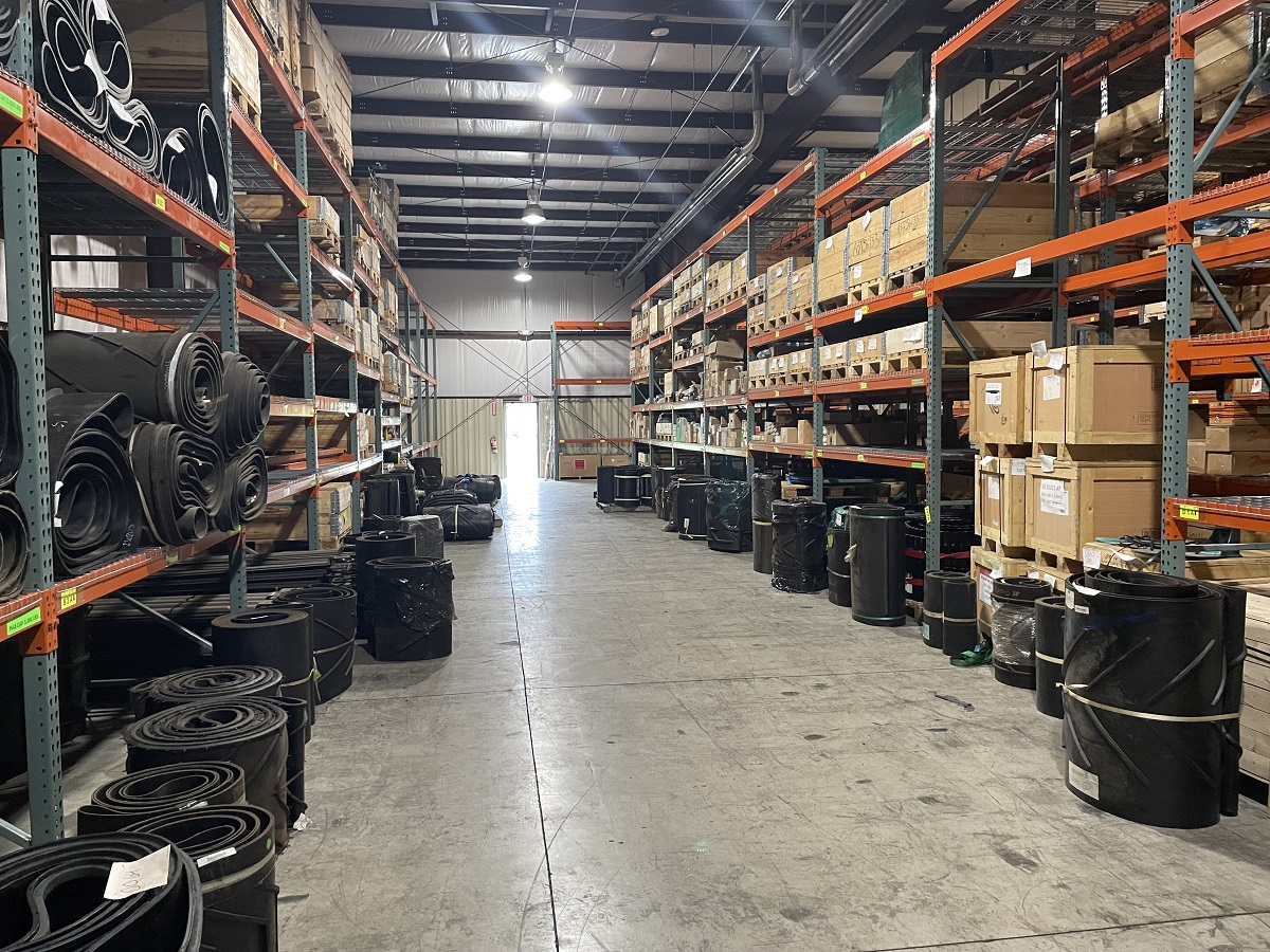 A view down a different aisle of parts. Rolled conveyor belts are seen as well as many crates.