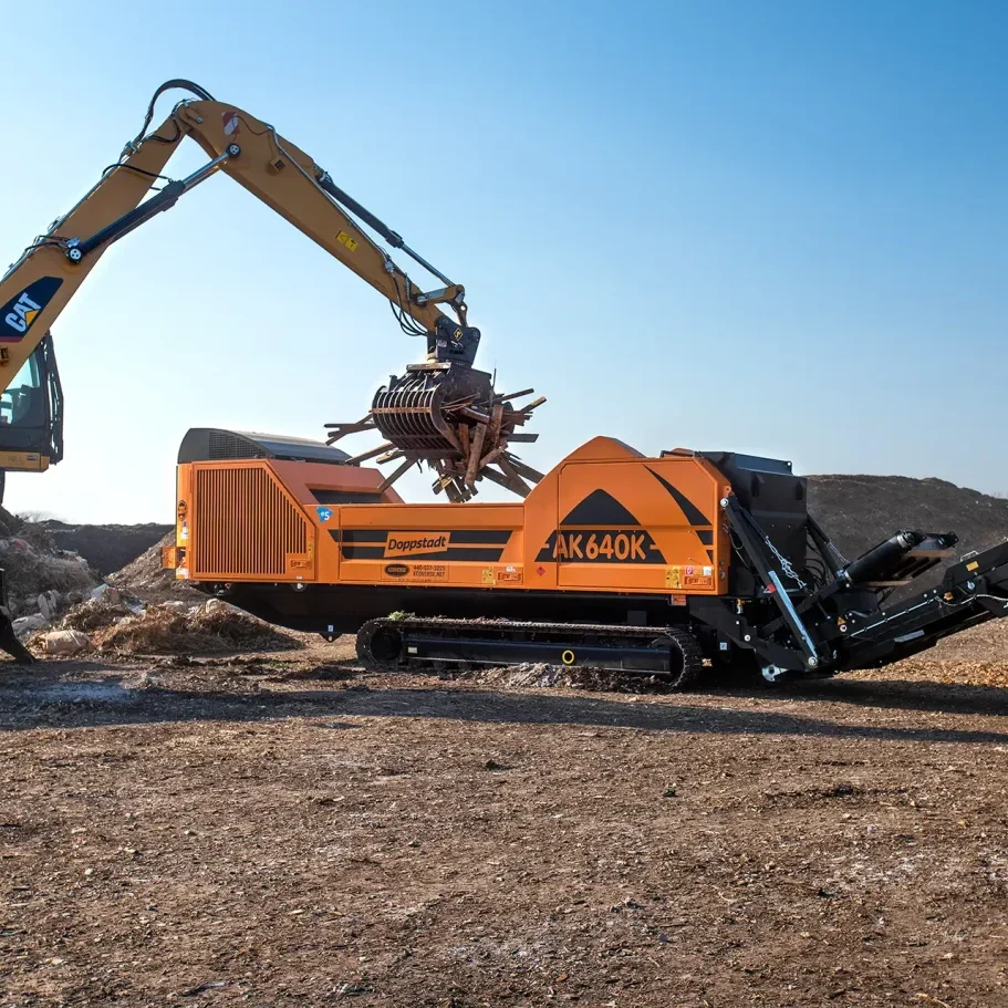 An orange Doppstant AK 640 grinder is loaded with waste wood to be ground into wood chips.