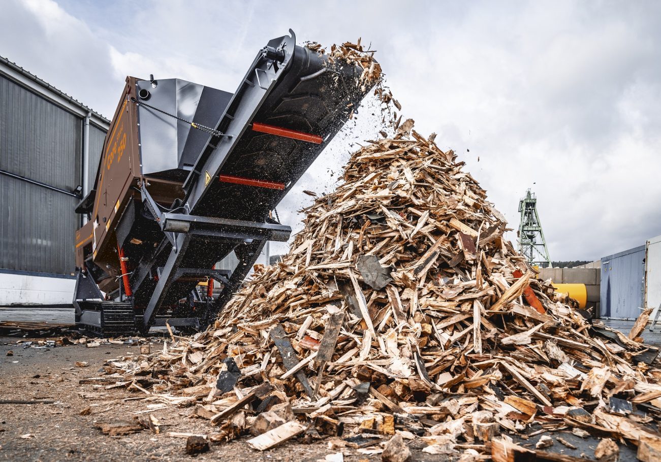 A CoreShred 250 shredder is seen from ground level as shredded wood is discharged from its main conveyor.