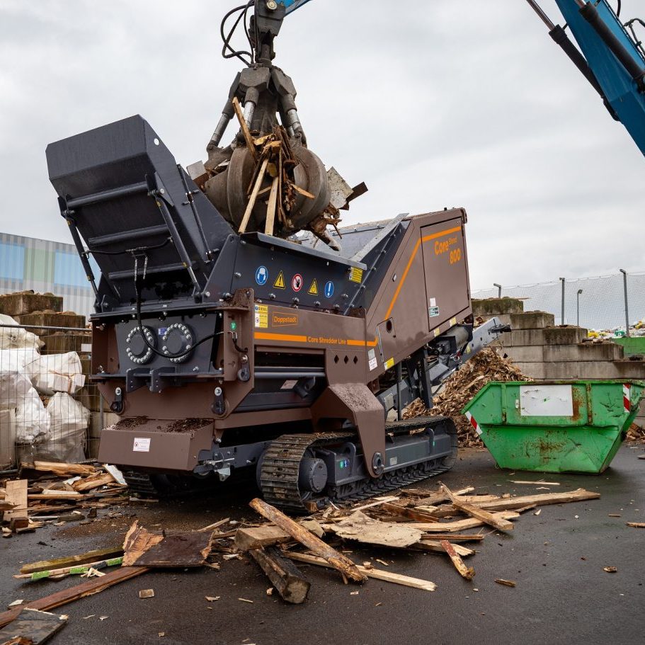 A crane is dropping waste materials into the hopper of a CoreShred 800 shredder.