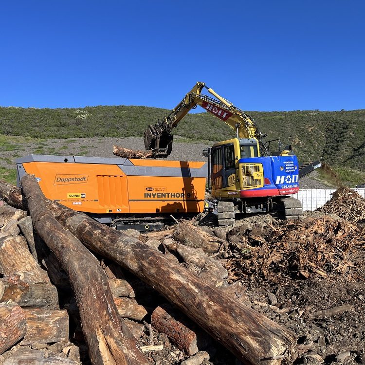 A high-torque shredder is loaded with large logs and stumps at a land clearing operation.