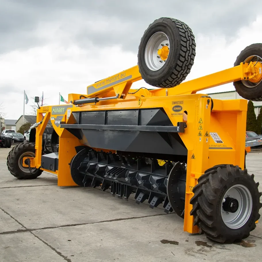 A Menart tow-behind compost turner is parked, showing its large and powerful rotating drum that turns compost windrows.
