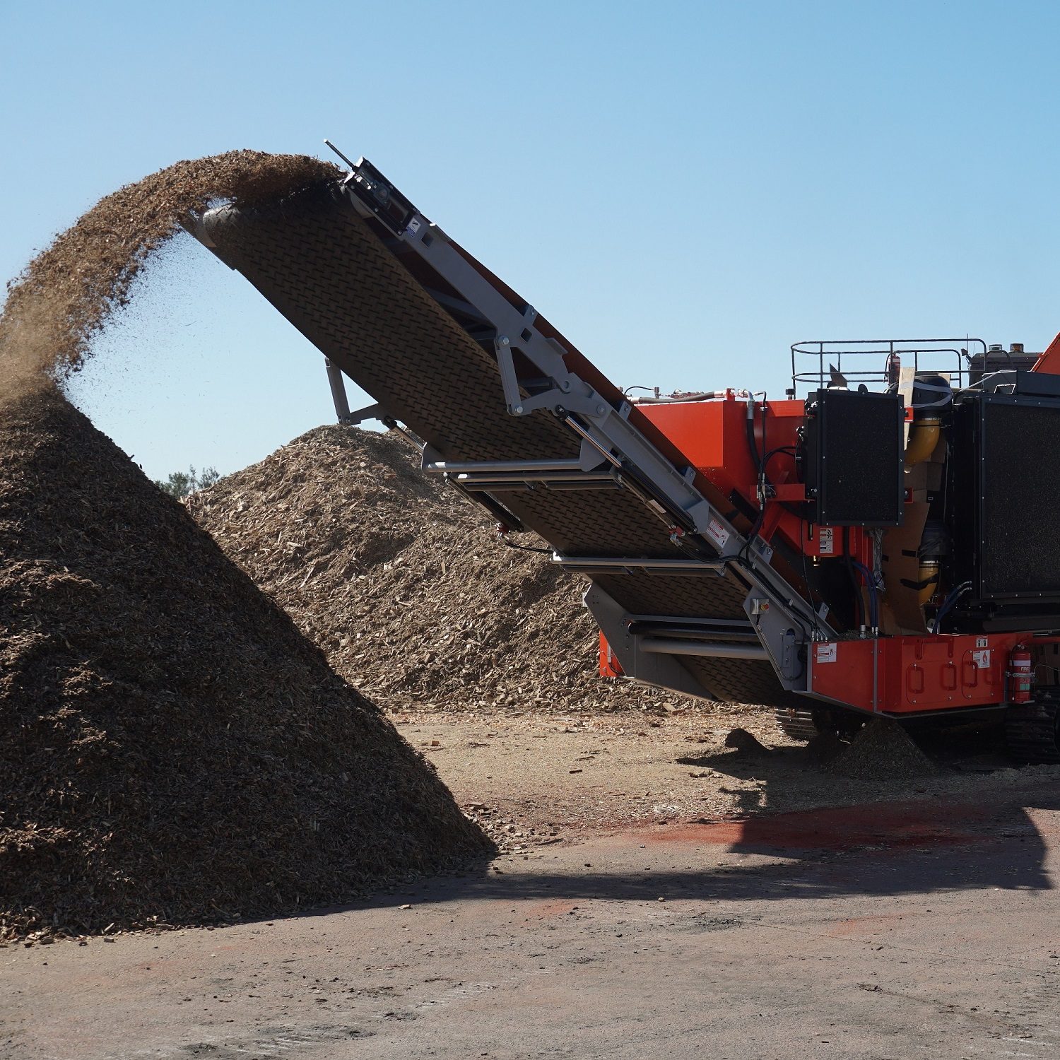A Redback grinder is seen from the front as wood chips roll off its conveyor into a large pile.