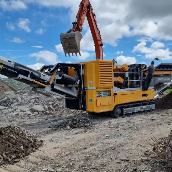 A black and amber Roco crusher is being fed rocks to be crushed into smaller rocks.
